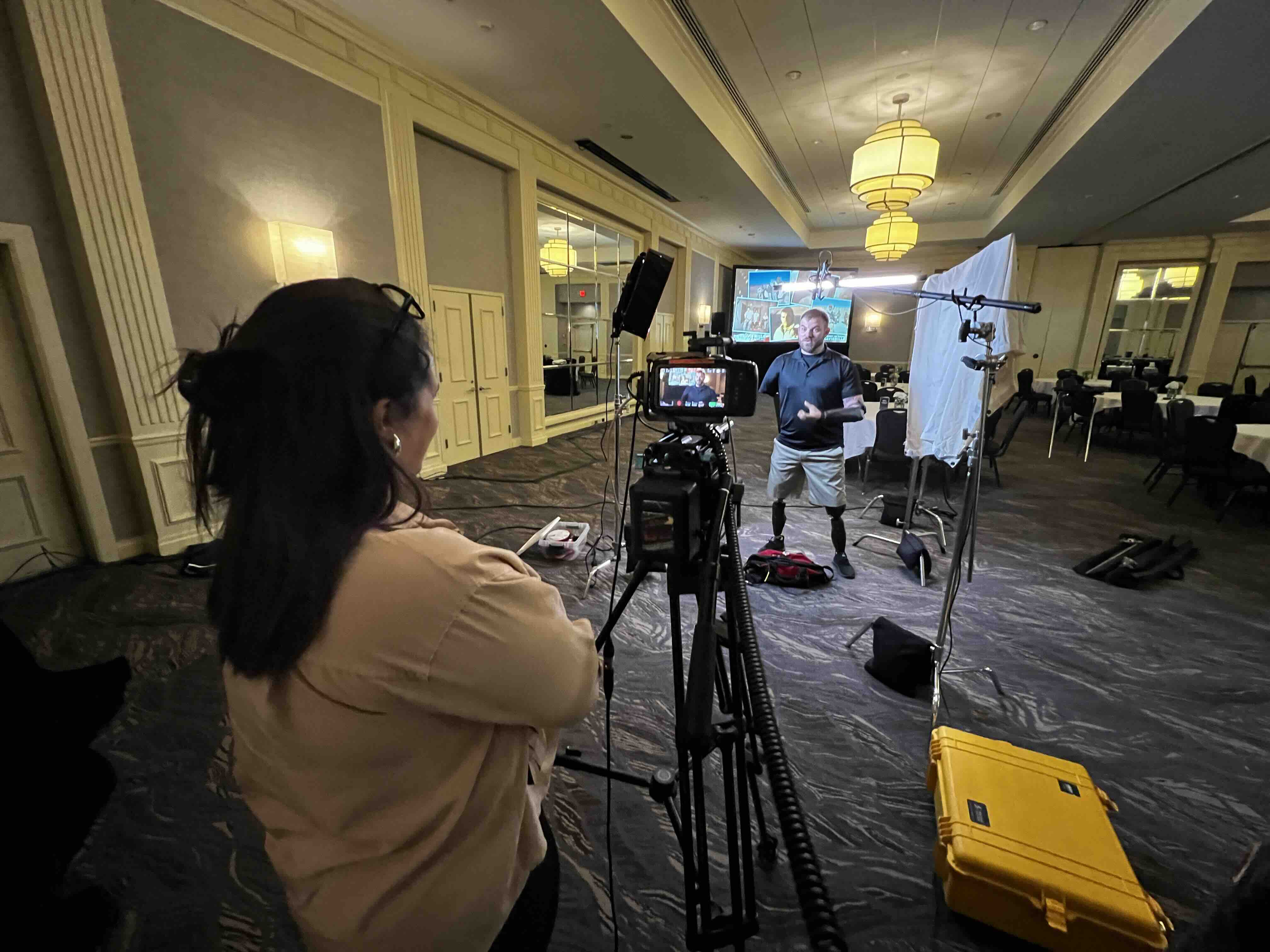 Interview production in a hotel ballroom, with a RetroMotion camera operator framing a standing speaker beside a presentation screen