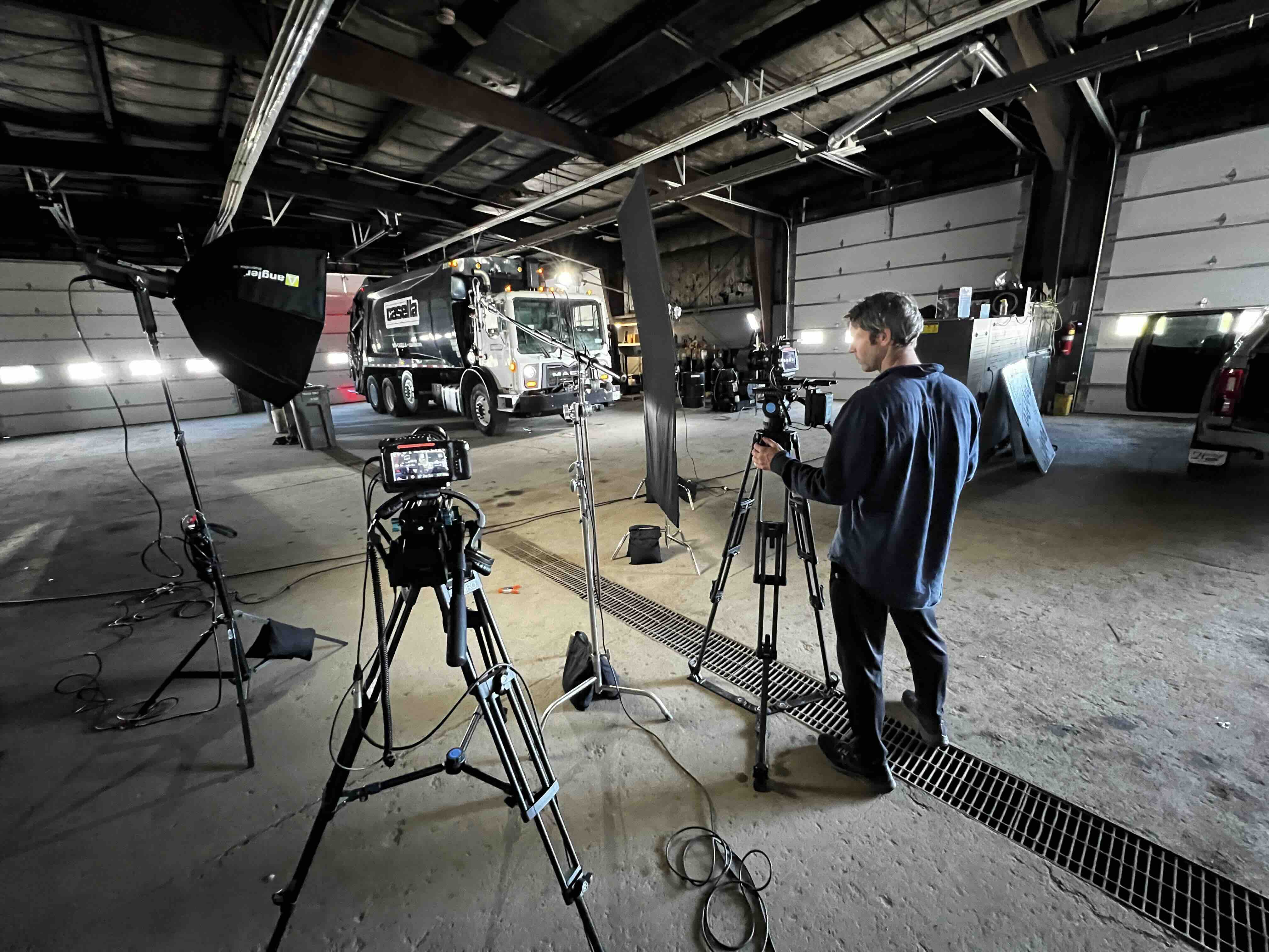Interview lighting and two cinema cameras set up around a company work truck inside a fleet garage, with a RetroMotion crew member adjusting the frame