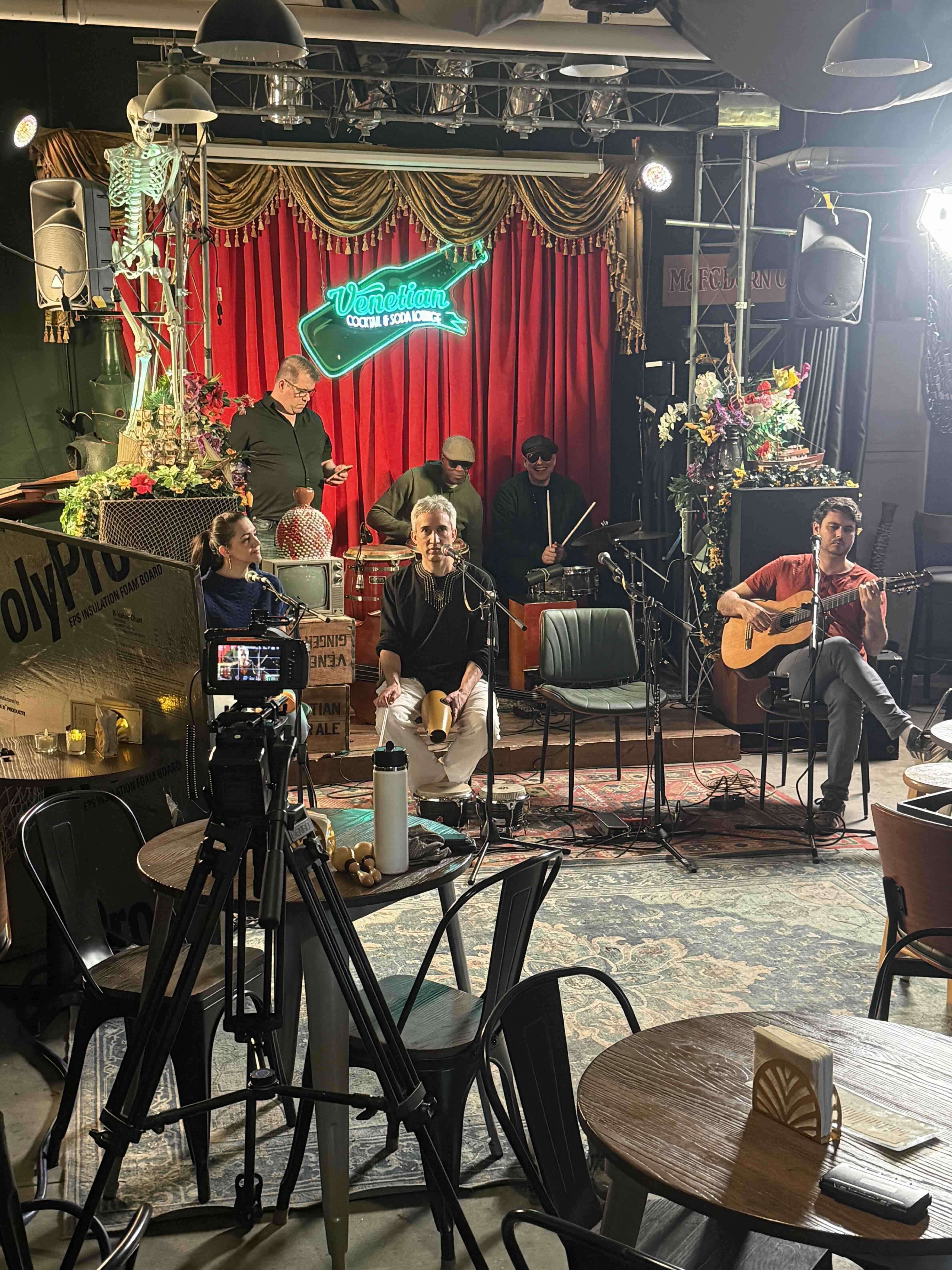 RetroMotion filming a live band on a cocktail lounge stage with a neon sign, red curtain, and stage lighting