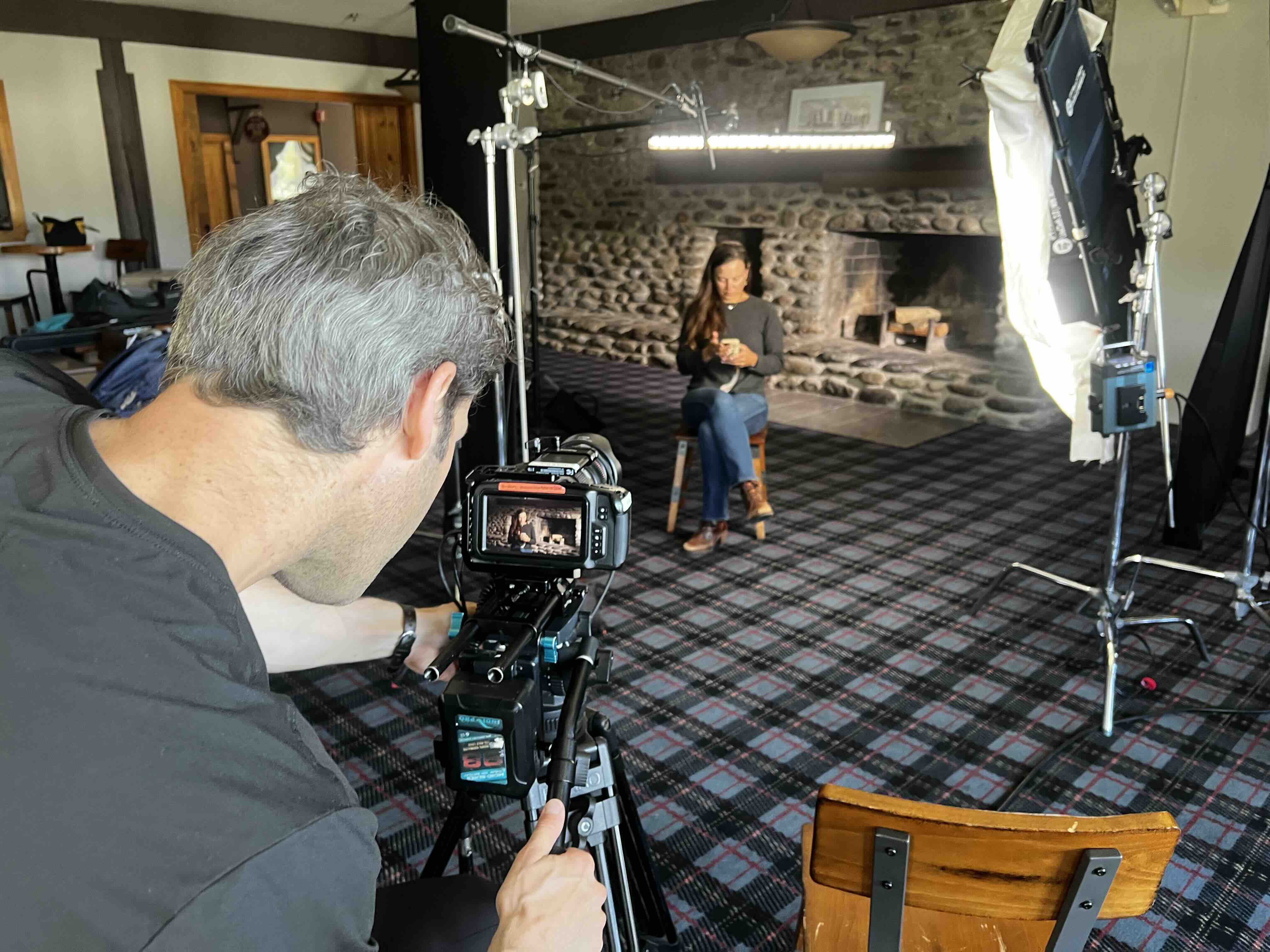 RetroMotion camera operator filming a seated interview beside a large stone fireplace in a rustic lodge great room