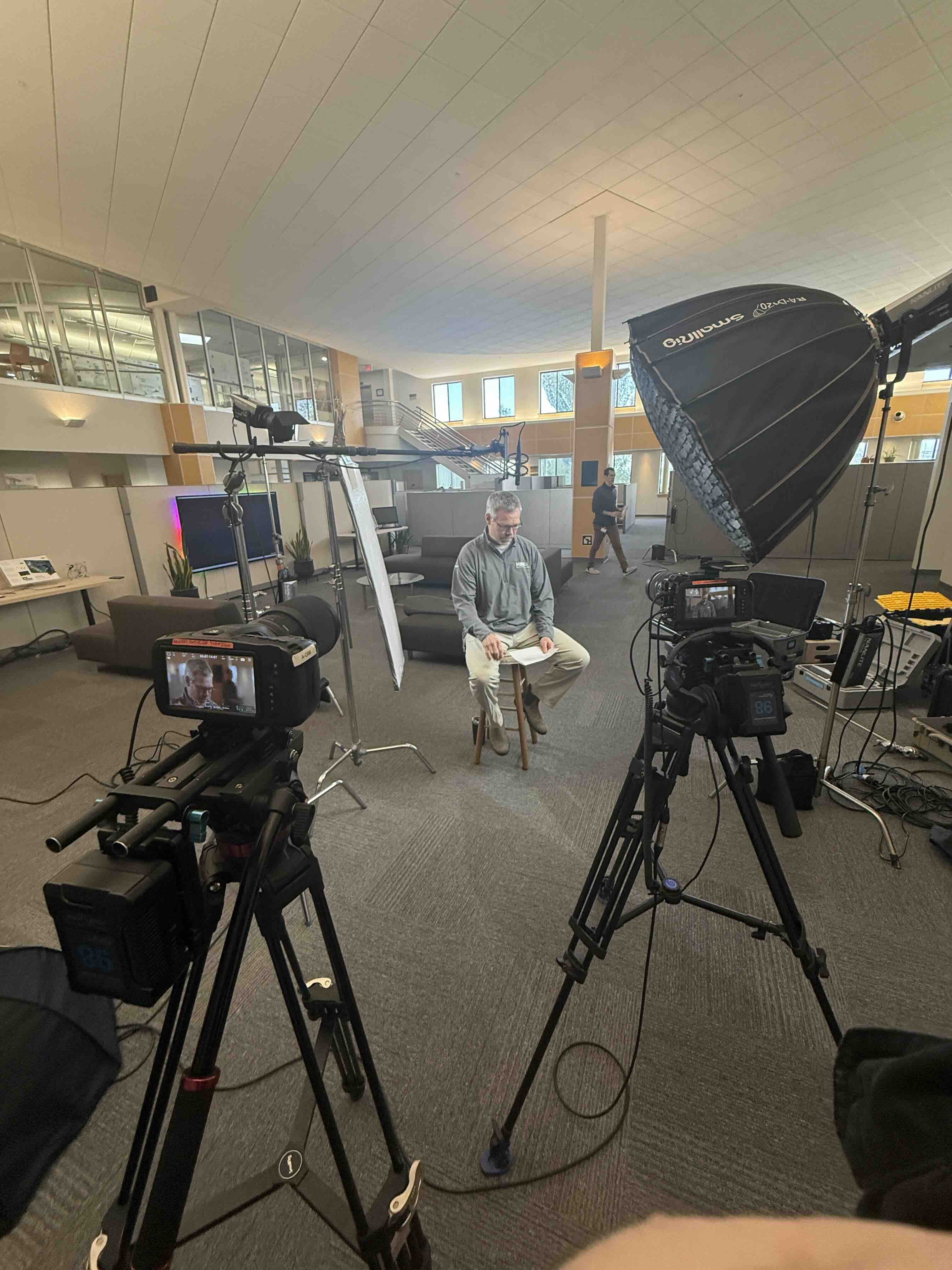 RetroMotion crew filming a two-camera corporate interview in a modern office atrium, with a large parabolic softbox and a subject seated on a stool